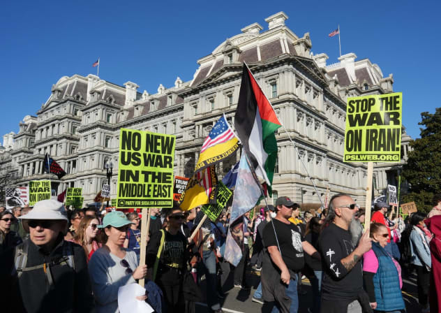People wave Iranian flags and signs condemning the war on Iran as they march past the Eisenhower Executive Building during a protest in Washington, DC, on February 28, 2026. 