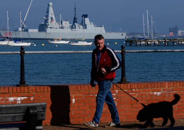 A man walks his dog as the HMS Dragon is undergoing ammunitioning operations at Upper Harbour Ammunitioning Facility (UHAF) in Portsmouth Harbour, March 4, 2026. 