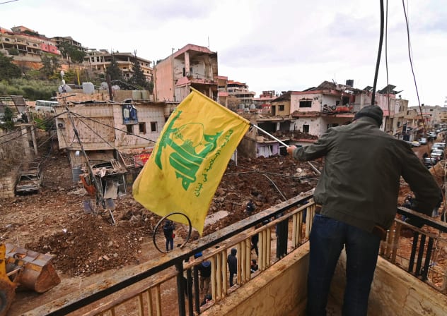 This photograph taken during a media tour organised by the Hezbollah shows a man installing a flag of Hezbollah on the balcony of a damaged building at Nabi Sheet town after an Israeli military operation in the Bekaa Valley of Lebanon, on March 7, 2026.