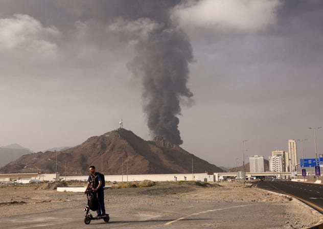 A person rides on a scooter as smoke rises in the Fujairah oil industry zone following a fire caused by debris after interception of a drone by air defenses, in Fujairah, United Arab Emirates, March 3, 2026