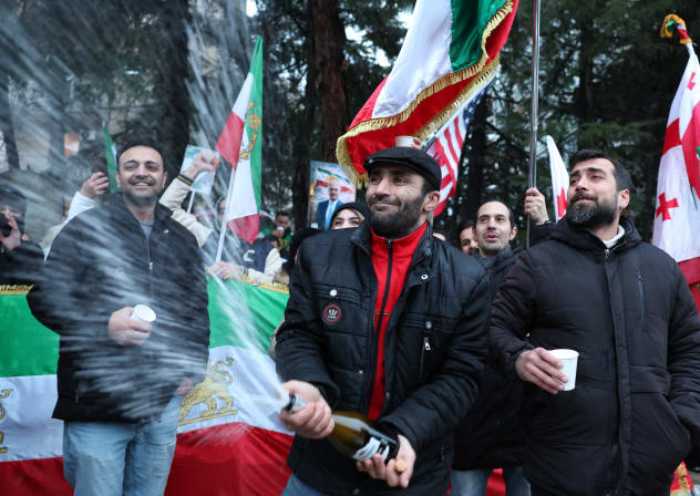 A member of the Iranian diaspora sprays a bottle of a sparkling beverage as they take part in a rally in front of the Iranian Embassy in Tbilisi on February 28, 2026, following the US and Israel's strikes on Iran.
