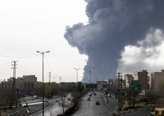 ars drive down a highway as smoke billows after overnight airstrikes on oil depots on March 8, 2026 in Tehran, Iran.