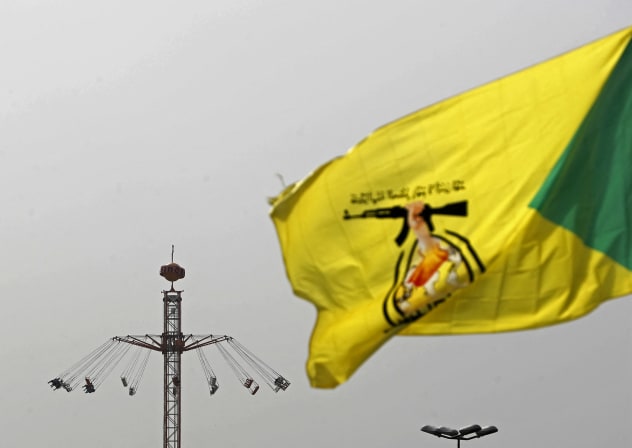A flag of Iraq's pro-Iran paramilitary group Hezbollah Brigades (Kataib Hezbollah), flutters against the backdrop of people taking a swing ride at an amusement park during Eid al-Fitr celebrations, marking the end of the Muslim holy fasting month of Ramadan, in Baghdad on March 21, 2026.