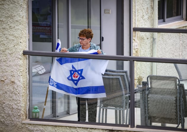 A woman holds an Israeli flag on a balcony near the scene where a missile fired from Iran struck a building in Haifa, northern Israel, as Israeli rescue forces recover bodies from the site, causing extensive damage, April 6, 2026. 