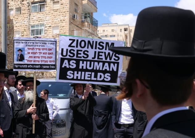 Ultra-Orthodox demonstrators holding a sign reading "Zionism uses Jews as human shields" outside of the IDF's recruitment offices in Jerusalem, April 12, 2026.