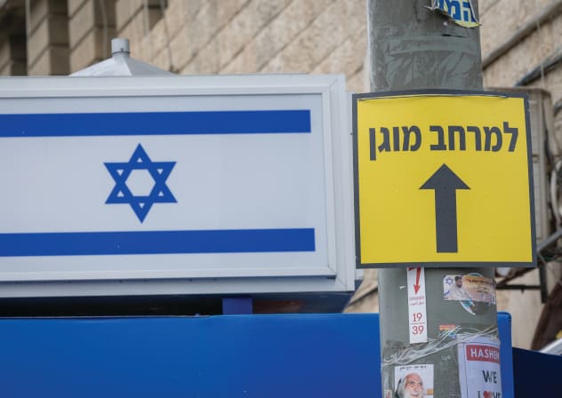 AN ISRAELI flag seen next to a sign pointing toward a protected space outside Mahaneh Yehuda Market in Jerusalem.