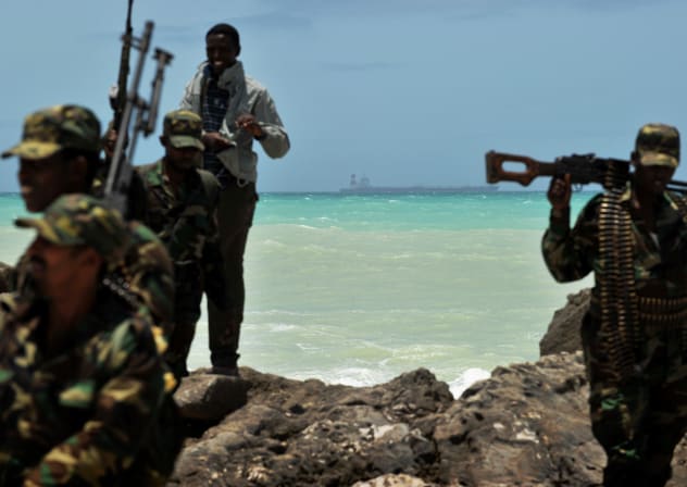 FILE PHOTO: Armed militiamen and a pirate walk on a rocky outcrop on the coast in the central Somali town of Hobyo as a a hijacked Korean supertanker lies anchored on the horizon on August 20, 2010.