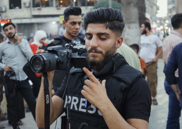 A journalist wearing a press vest holds his camera during a protest in Idlib, Syria on August 11, 2025.