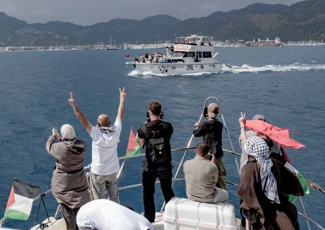 People raise V-signs and take photos from a boat decorated with Palestinian flags as another vessel displaying solidarity signs sails past near the port in Marmaris, Turkey, on May 14, 2026.
