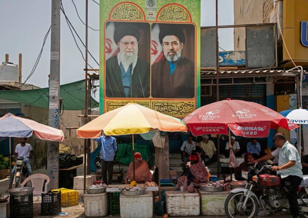 Food vendors sit below posters of the former Supreme Leader Ali Khamenei and the current Supreme Leader Mojtaba Khamenei on May 17, 2026 along the Strait of Hormuz in, on Qeshm Island, Iran. 
