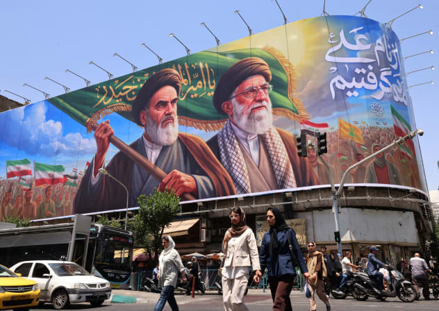 People cross the street past a large billboard showing portraits of Iran's late supreme leader, Ayatollah Ruhollah Khomeini (L) and slain supreme leader Ayatollah Ali Khamenei (R) in central Tehran on June 8, 2026.