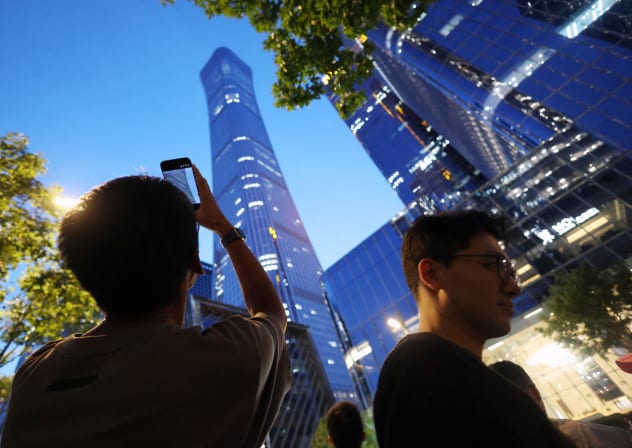 A man points a mobile phone at CITIC Tower, also known as China Zun, where damage is visible on a high floor of the exterior, in Beijing, China June 26, 2026. 