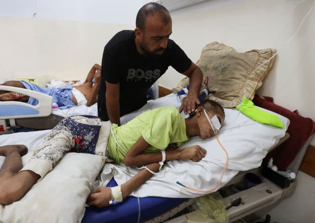 Injured Palestinian Hassan Qlob, 18, who his father says was shot in the head more than two months ago while out seeking food, lies on a bed as he waits for the Rafah crossing to reopen so he can receive treatment abroad, as his father Ibrahim tends to him, after the Israel-Hamas ceasefire.