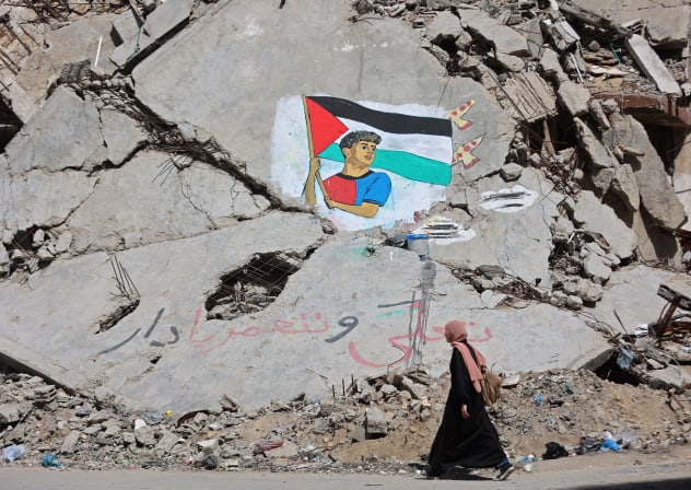 A woman walks past a mural depicting football player Lamine Yamal waving a Palestinian flag during the Catalans' title parade, painted by Palestinian artists on the rubble of buildings destroyed during the war, at Shati (Beach) refugee camp in Gaza City on May 13, 2026.