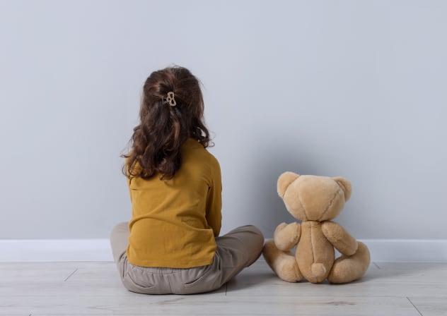 Little girl with teddy bear near light wall indoors, back view
