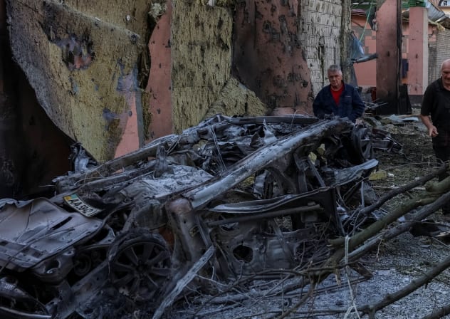 Residents look at a burned car at a site of a Russian missile strike, amid Russia's attack on Ukraine, in Kyiv region, Ukraine August 1, 2026. 
