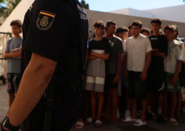 A police officer stands guard as migrant children queue outside a police station to be registered following mass crossings by migrants on foot and by sea from Morocco into Spanish territory, in Ceuta, Spain, August 6, 2026. 