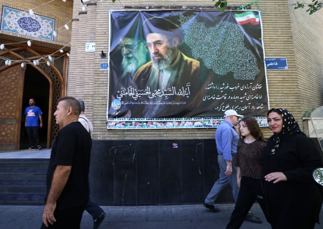 Iranians walk past a mosque decorated with a banner depicting Iran's current leader Ayatollah Mojtaba Khamenei, in the capital Tehran on May 9, 2026.