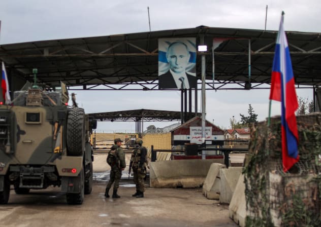A portrait of Russia's President Vladimir Putin hangs above as Russian military trucks enter the Russian-leased Syrian military base of Hmeimim in Latakia province in western Syria on December 29, 2024. 