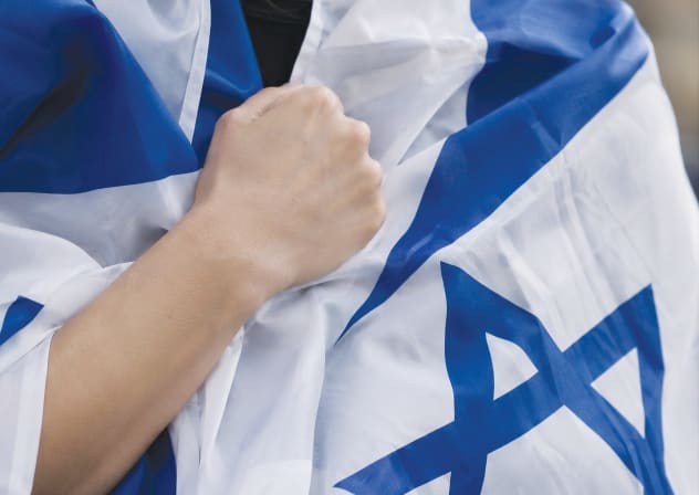 An individual clothed in an Israeli flag recites the Yom Kippur vidui prayer, beating their chest. 