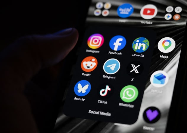 This photograph shows a set up smart-phone screen displaying the logo of main social media platforms including Instagram, Facebook, LinkedIn, Reddit, Telegram, X, Bluesky, Tiktok and Whatsapp.