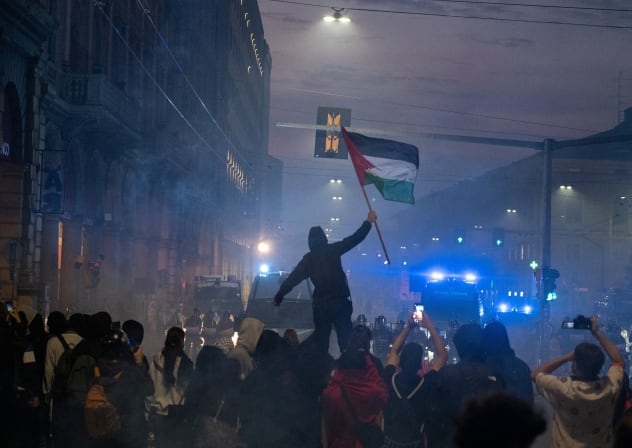 A demonstrator waves a Palestinian flag as protesters face police amid smoke during clashes following a protest against the rising cost of living in Bologna, Italy, October 17, 2026.