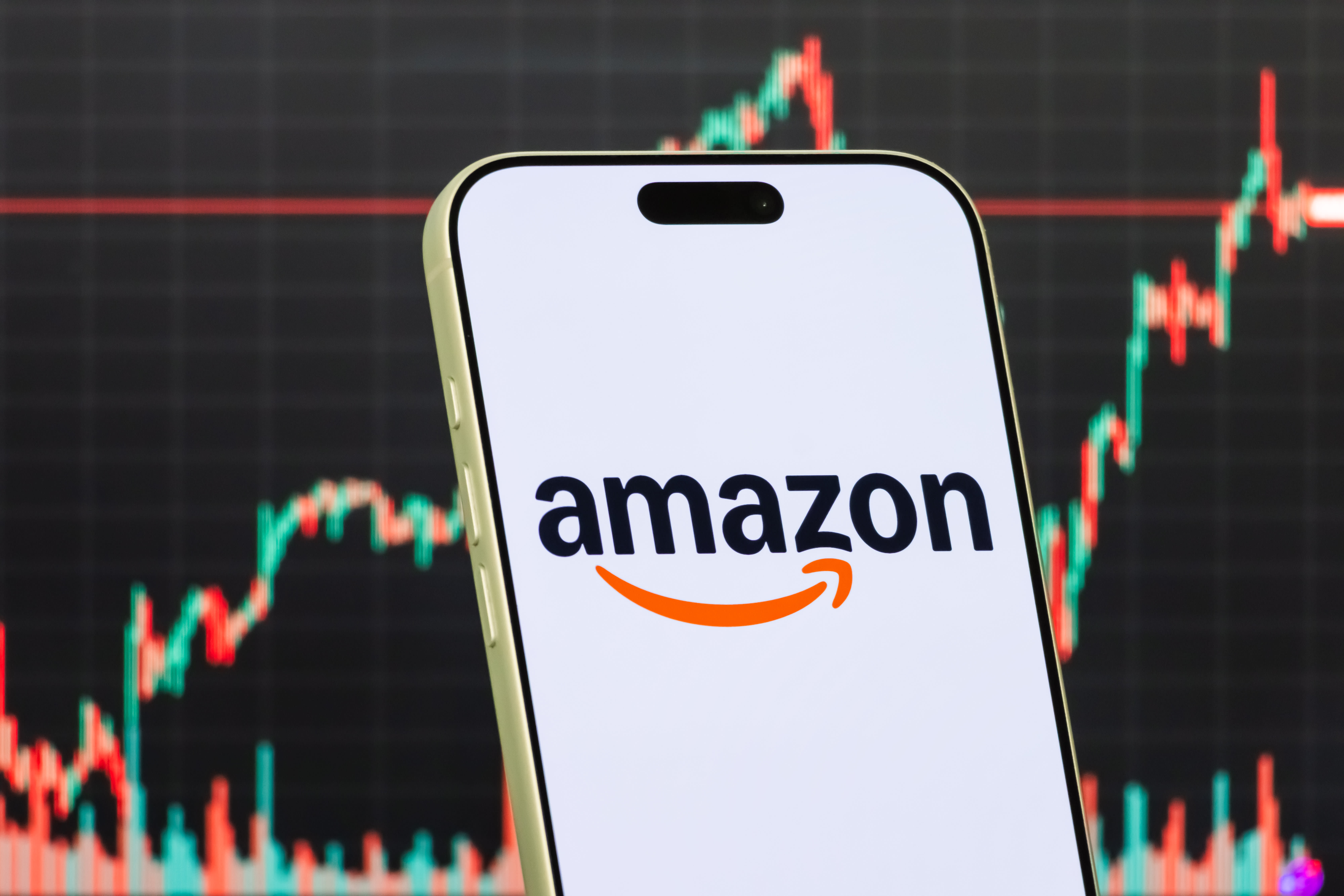 A smartphone displays the Amazon logo in front of a screen showing the company