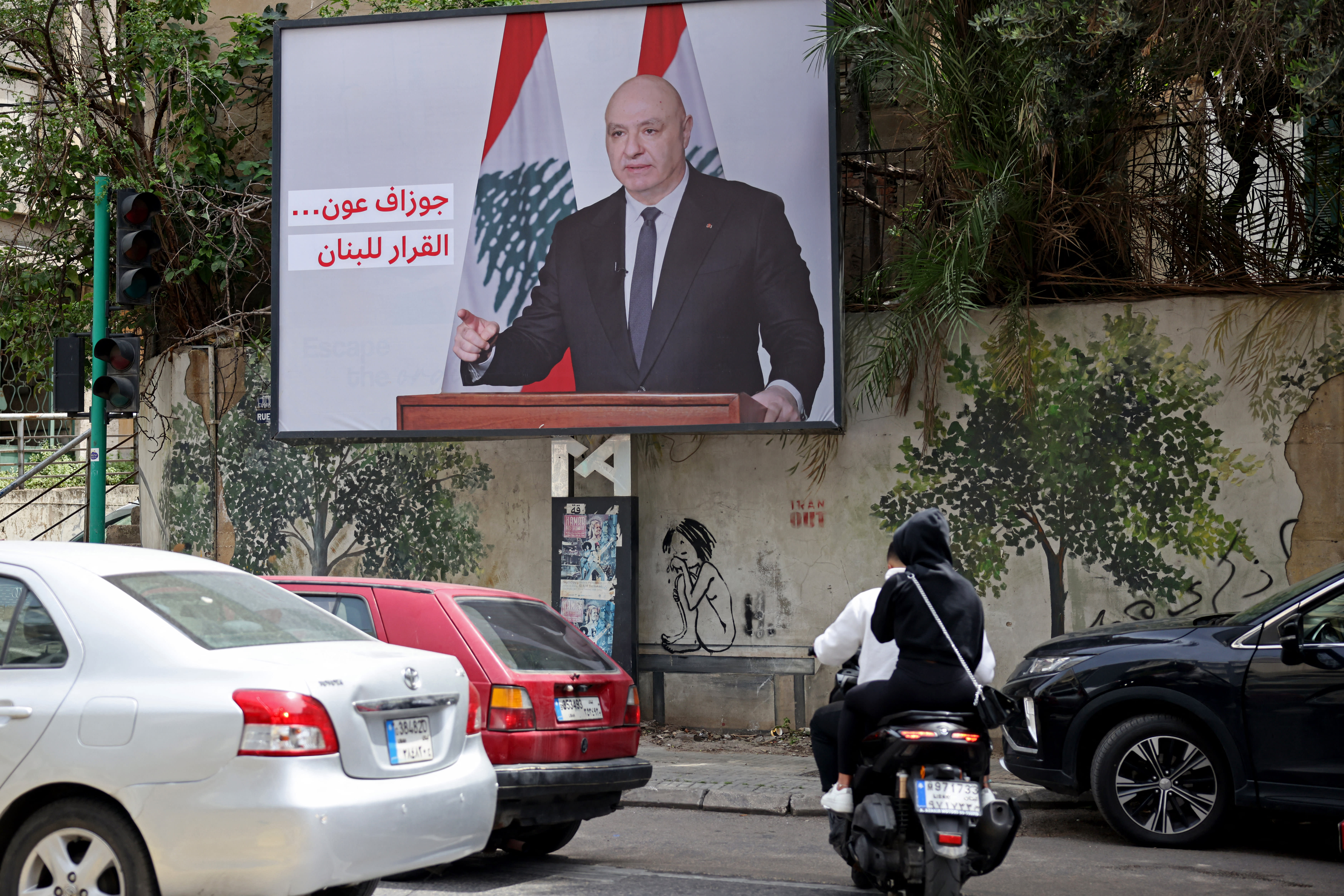 Vehicles drive past a billboard depicting Lebanon