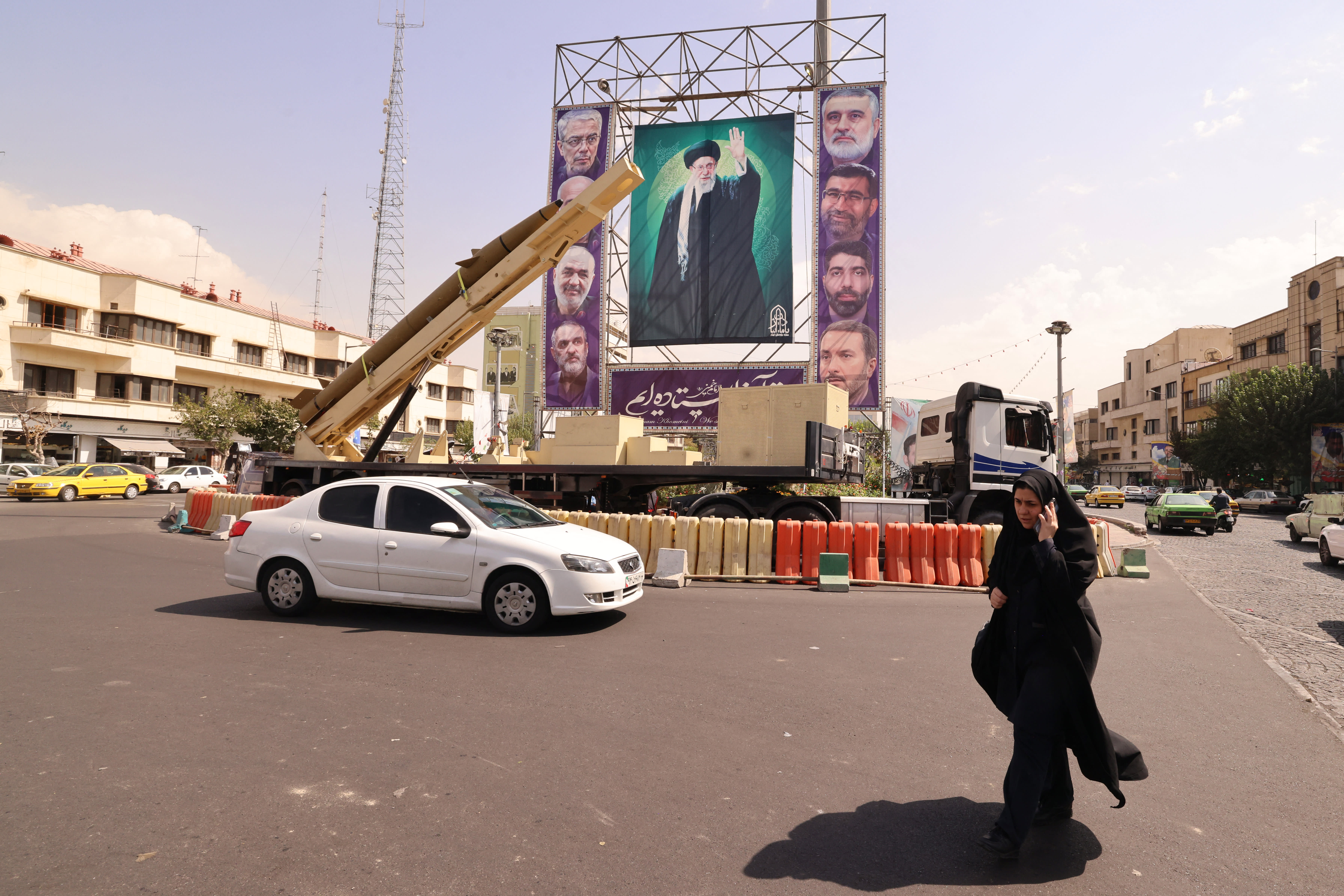 A woman walks past a deactivated Kheibar Shekan ballistic missile in front of a picture of Iran