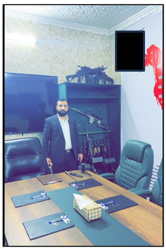 MOHAMMAD BAQER Saad Dawood Al-Saadi standing in front of an array of machineguns in a conference room. (photo credit: US Justice Department Office of Public Affairs)