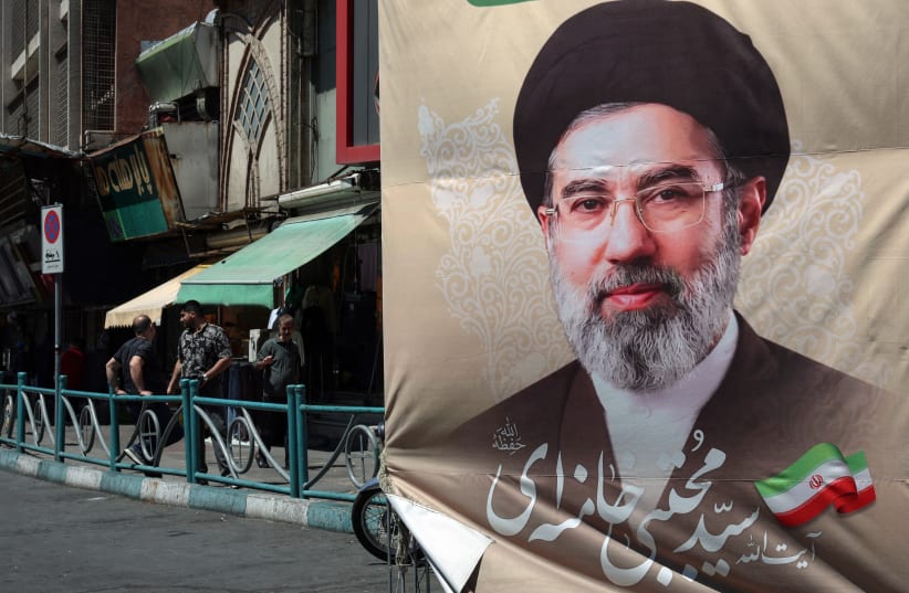 Iranians stand on a pavement along a street next to a billboard depicting Iran