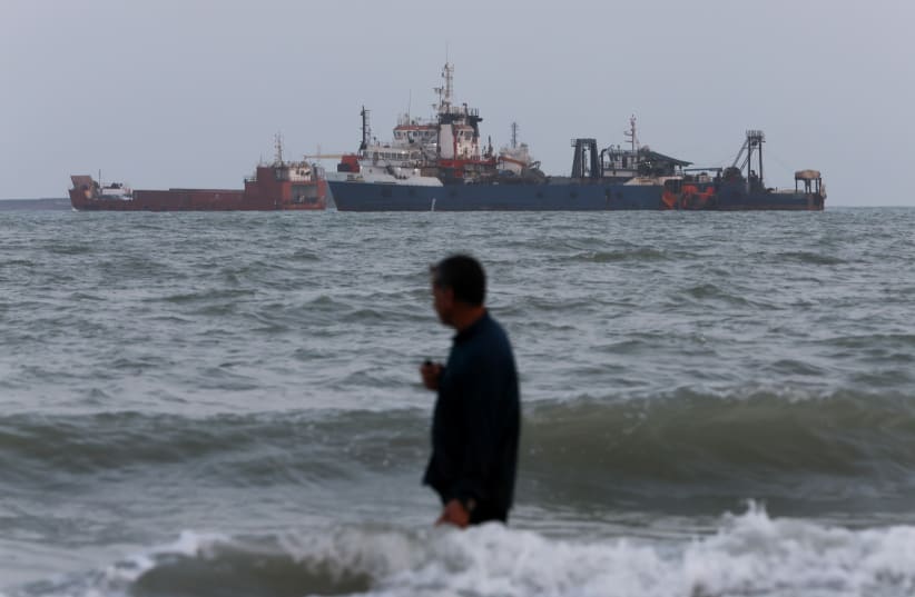 A person wades in the water as ships are seen anchored in the Strait of Hormuz on August 10, 2026 off the coast of Bandar Abbas, Iran.
