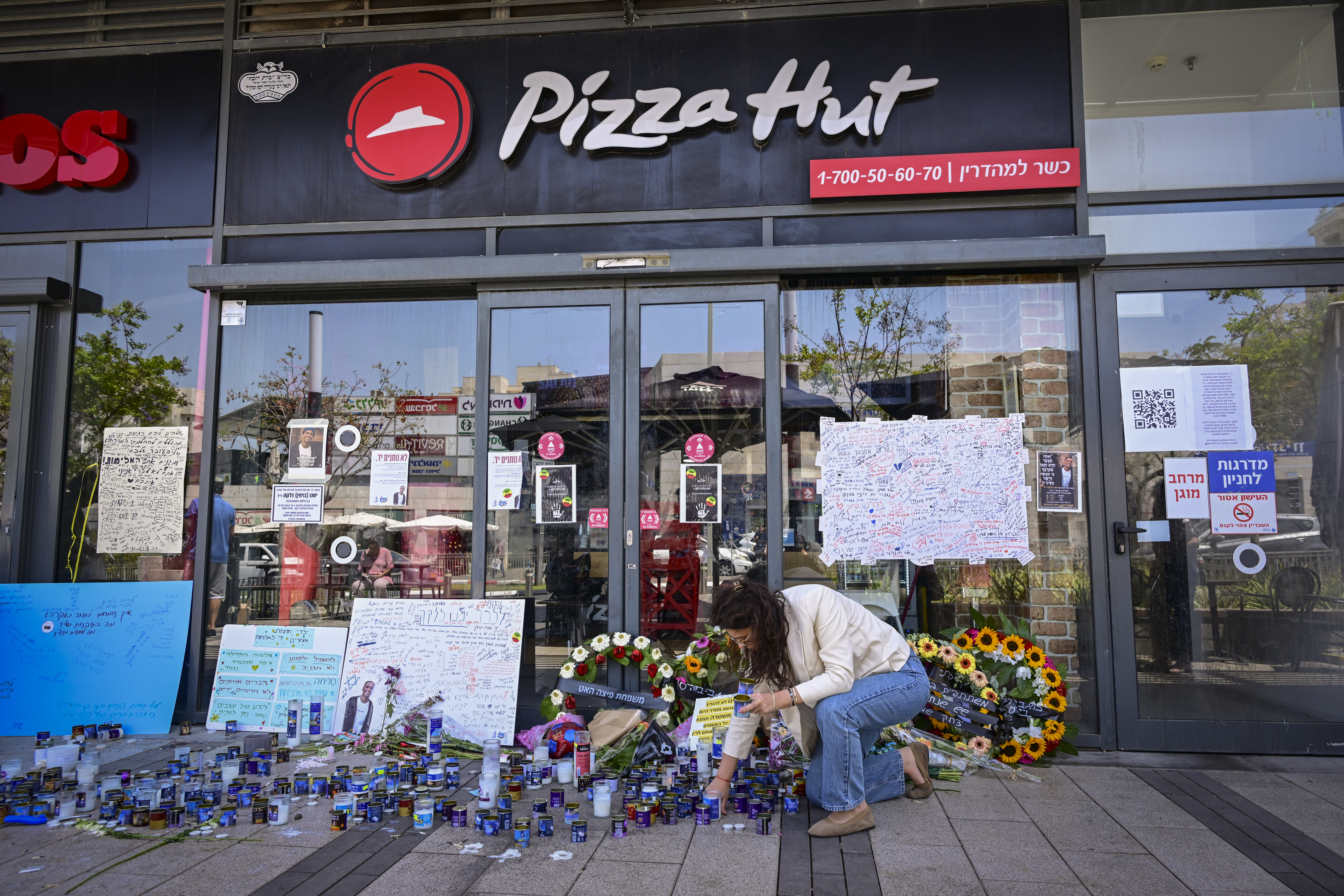 People gather outside a Pizza Hut branch in Petah Tikva, lighting candles and placing flowers in memory of employee Yemanu Binyamin Zalka, who was stabbed and later died of his wounds on the eve of Independence Day, April 27, 2026 (photo credit: AVSHALOM SASSONI/FLASH90)