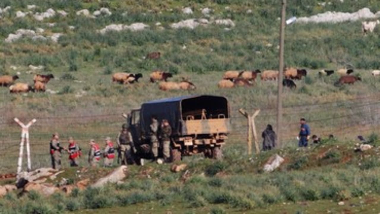 Turkish soldiers stand guard as Syrian refugees cross border