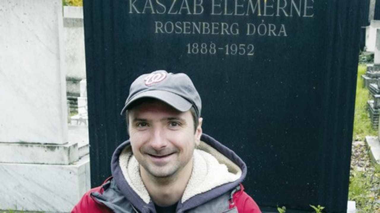 Gabor Banfalvi, who was raised Catholic, poses in front of a tombstone that bears his mother’s maiden name in a Jewish cemetery.
