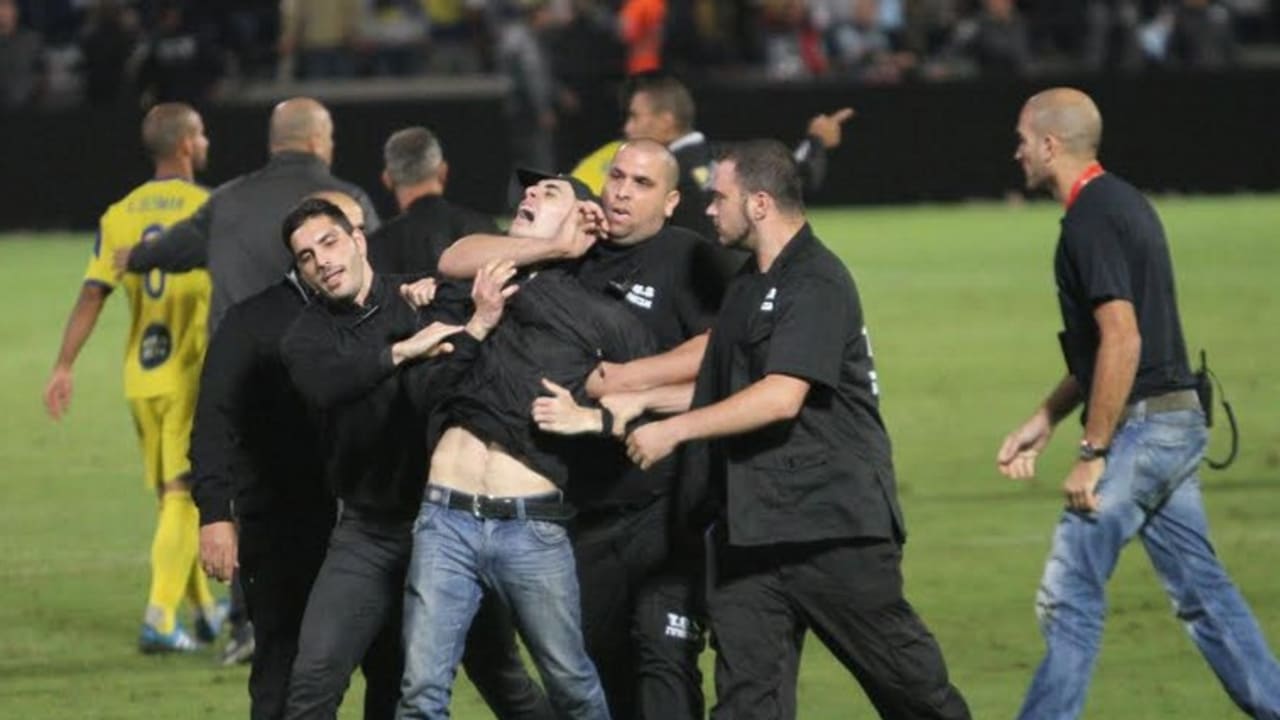 Security guards haul away a fan who ran onto the pitch