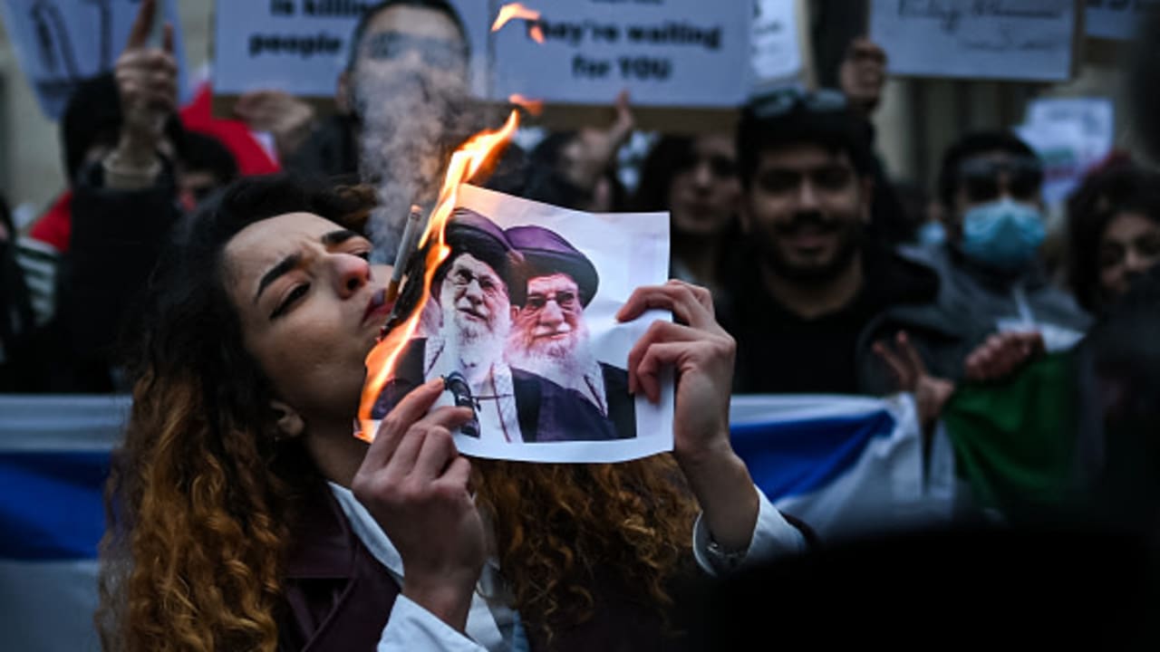 An anti-Iranian regime protester lights a cigarette with a lit paper depicting Ali Khamenei, Supreme Leader of Iran during a gathering outside the US Consulate in Milan, on January 13, 2026.