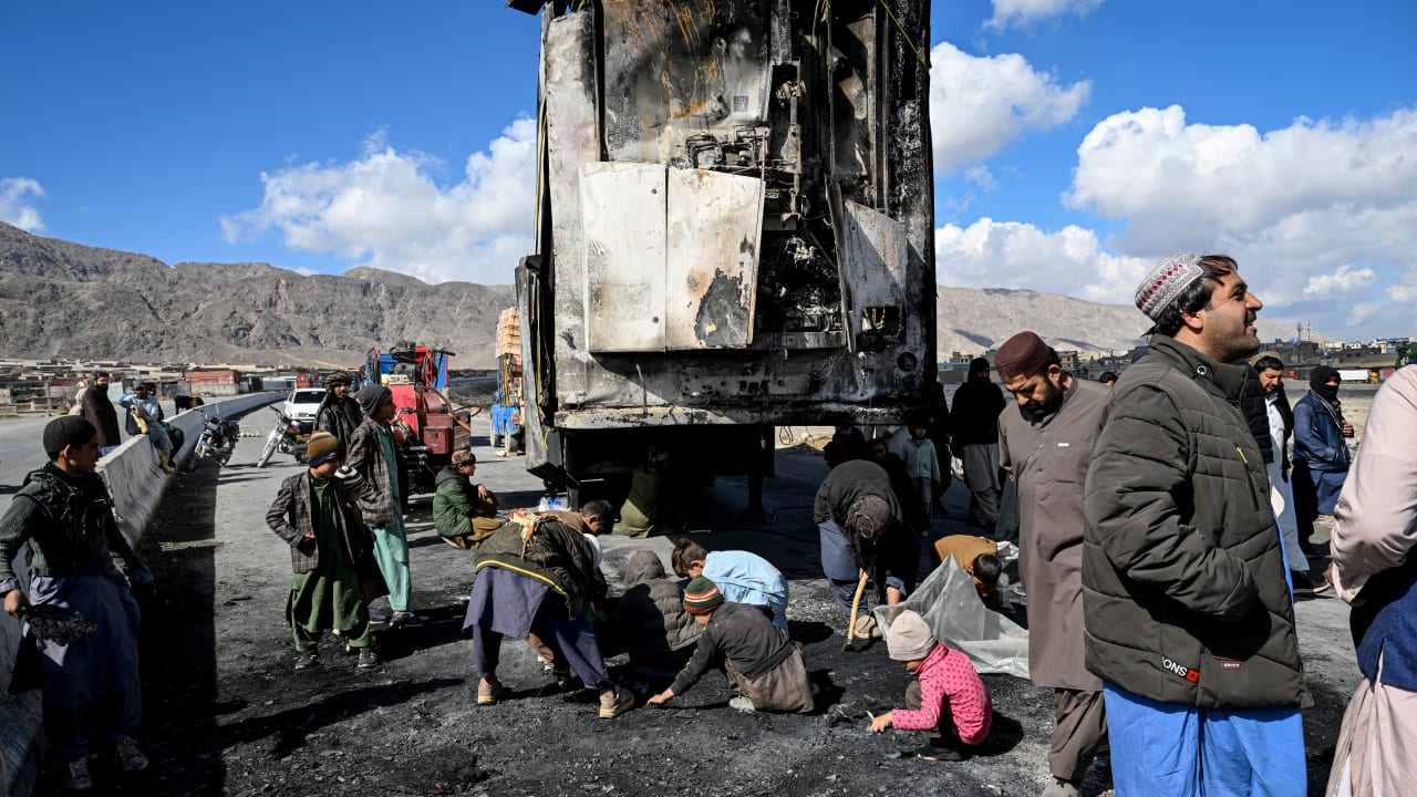 People gather as others collect recyclable items beside a burnt vehicle along a road on the outskirts of Quetta on February 1, 2026 a day after an attack by Baloch separatists. 