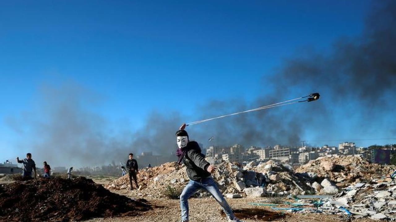 Un palestino lanza piedras con una honda durante los enfrentamientos con las tropas israelíes cerca del asentamiento judío de Beit El, cerca de Ramala, en la Cisjordania ocupada por Israel, el 14 de diciembre de 2018. 