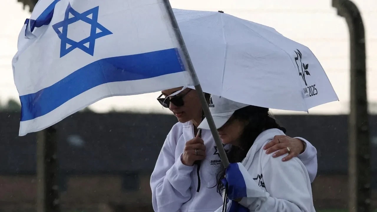 Una mujer sostiene una bandera israelí y otra persona la protege de la lluvia durante la Marcha de los Vivos en Auschwitz-Birkenau en abril. Nacidos en el pacto posterior a Auschwitz, considerábamos que el odio hacia los judíos era algo pasado, condenado al fracaso, como el racismo