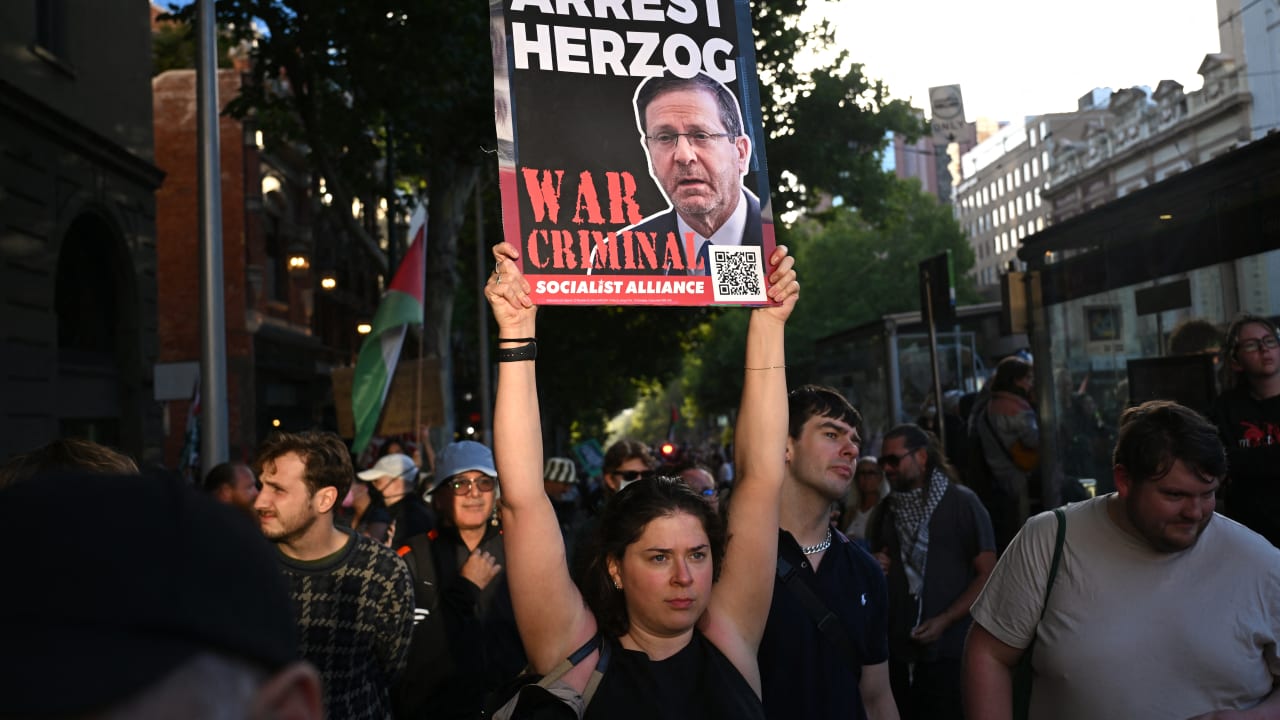 A protester holds aloft a placard as they march during the visit of Israel's President Isaac Herzog in Melbourne on February 12, 2026