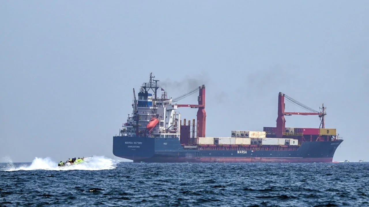 Una embarcación se aproxima al buque portacontenedores Marsa Victory, con bandera de San Cristóbal y Nieves, mientras navega por las aguas del estrecho de Ormuz, frente a la costa de Khasab, en la península de Musandam, al norte de Omán, el 25 de junio de 2025. 