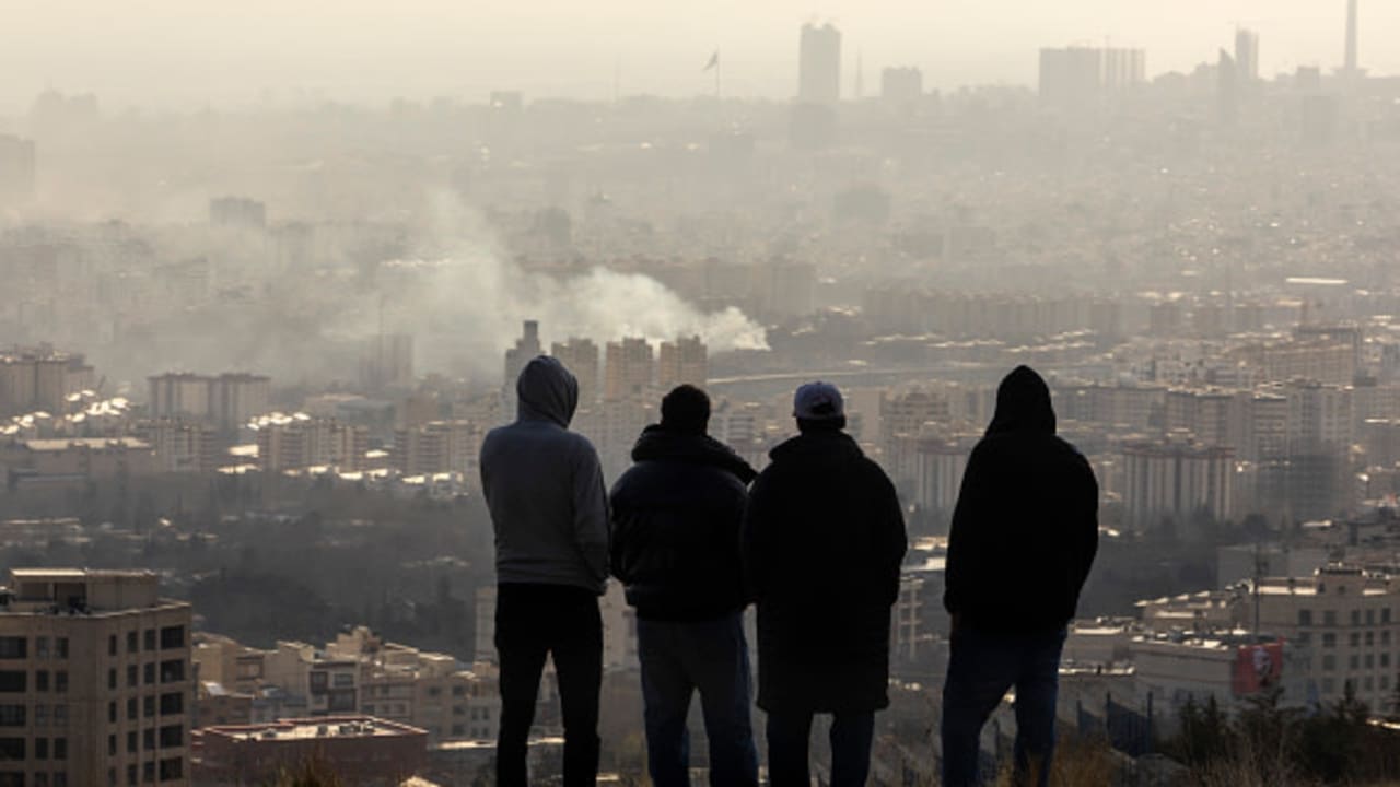 Men watch from a hillside as a plume of smoke rises after an explosion on March 2, 2026 in Tehran, Iran. 