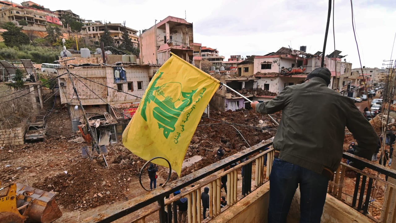 This photograph taken during a media tour organised by the Hezbollah shows a man installing a flag of Hezbollah on the balcony of a damaged building at Nabi Sheet town after an Israeli military operation in the Bekaa Valley of Lebanon, on March 7, 2026.