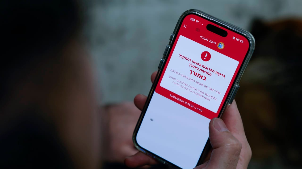 A man shows a missile alert notification on his mobile phone as residents take cover indoors following missile fire from Iran toward Israel, in Mishmar David, March 10. 2026.