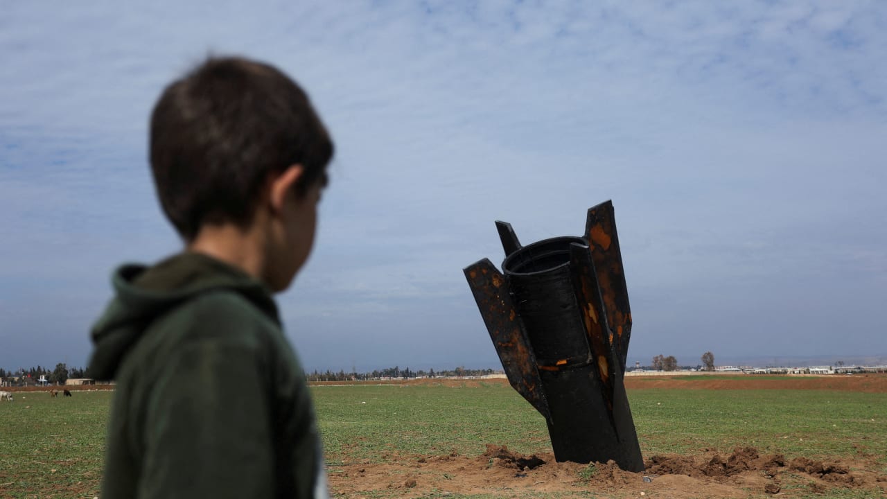 A child stands next to a missile after it fell near Qamishli International Airport, amid the US-Israeli conflict with Iran, in Qamishli, Syria, March 4, 2026.