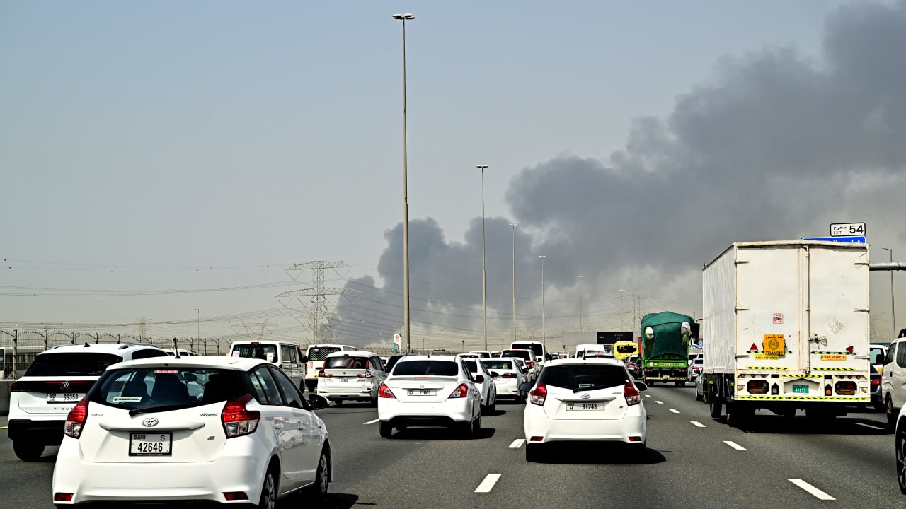 Smoke billows from an ongoing fire near Dubai International Airport as vehicles drive on a highway in Dubai on March 16, 2026.