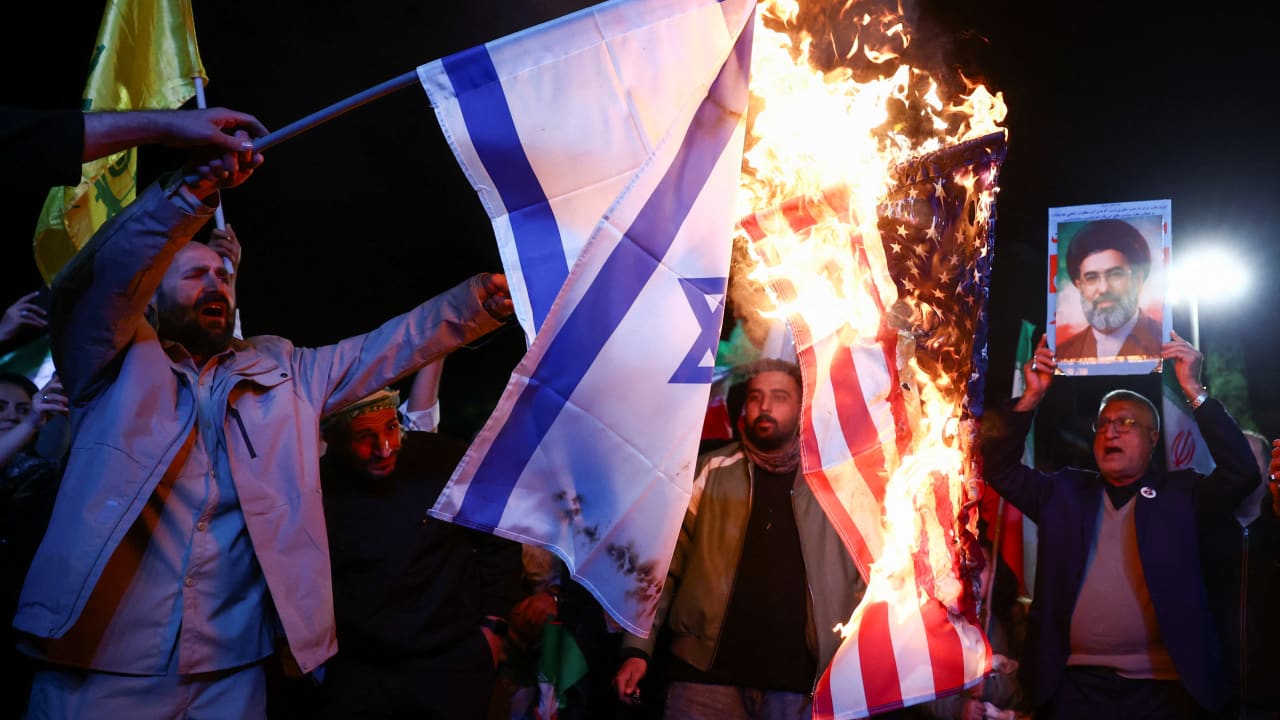 A man holds a photo of Iran's Supreme Leader, Mojtaba Khamenei, while the flags of the US and Israel are burnt, as people gather after a two-week ceasefire in the Iran war was announced, in Tehran, Iran, April 8, 2026. 