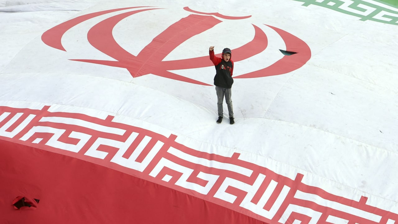 A boy raises his fist while standing on a giant Iranian flag during the funeral of Alireza Tangsiri, commander of the Iranian Revolutionary Guards' navy, alongside others killed in US-Israeli strikes on Iran at Enghelab Square in Tehran on April 1, 2026. 