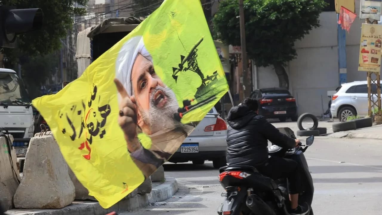 Una persona que circula en scooter lleva una bandera con la imagen del líder de Hezbolá, Naim Qassem, mientras los desplazados se dirigen a sus hogares tras la entrada en vigor de un alto el fuego de diez días entre el Líbano e Israel, en los suburbios del sur de Beirut, Líbano. 